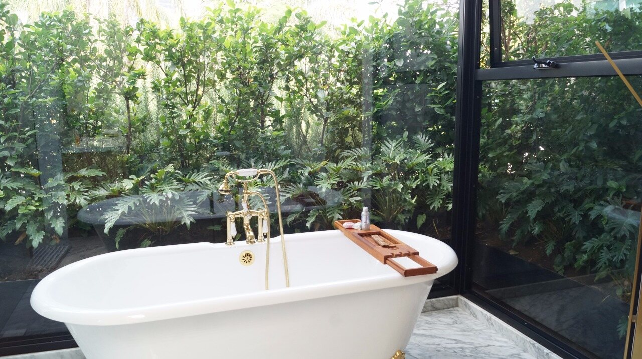 A freestanding tub in a glass conservatory surrounded by lush planting.