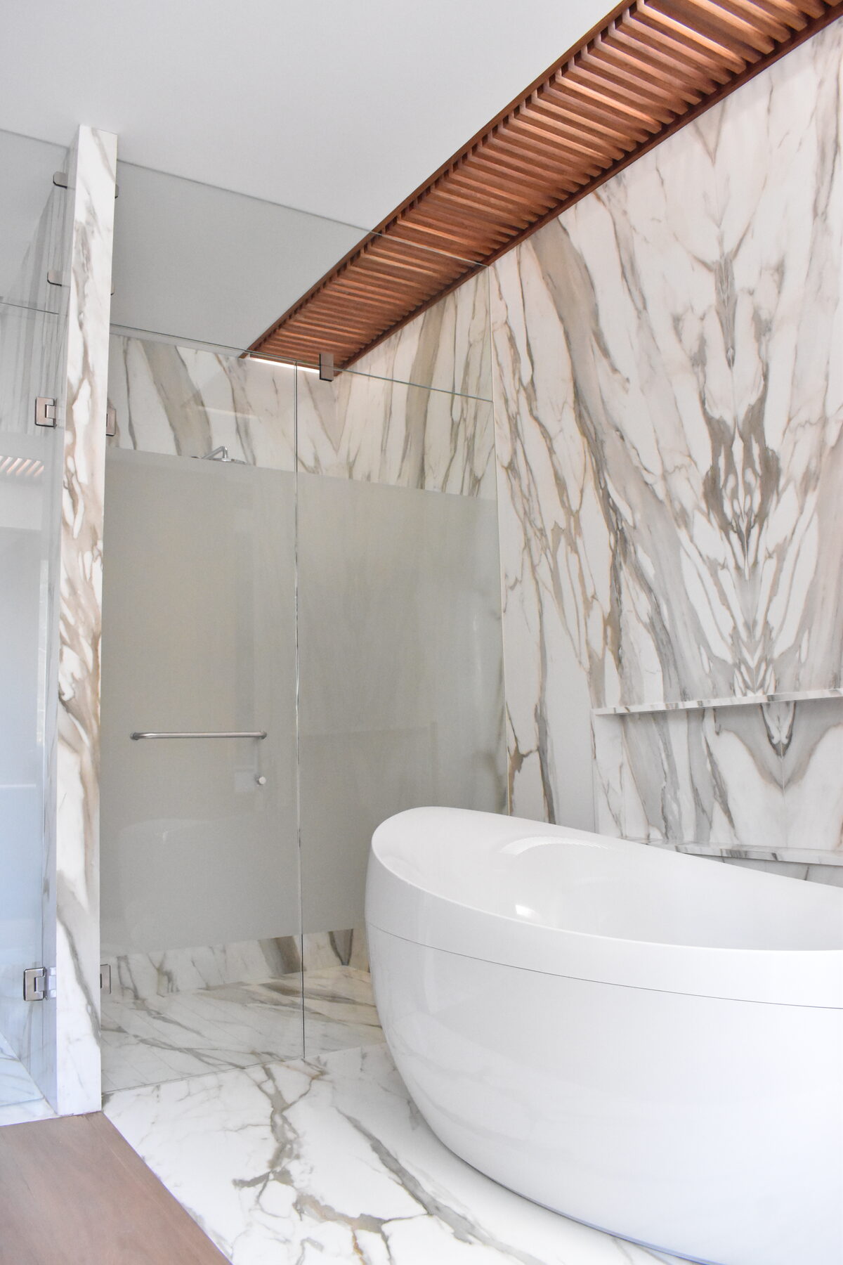 A bathroom lined in book-matched marble with a freestanding tub.
