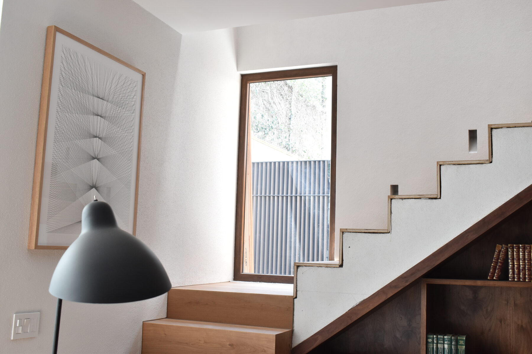 A stair beside a framed drawing and reading lamp, lit by a timber-framed window.