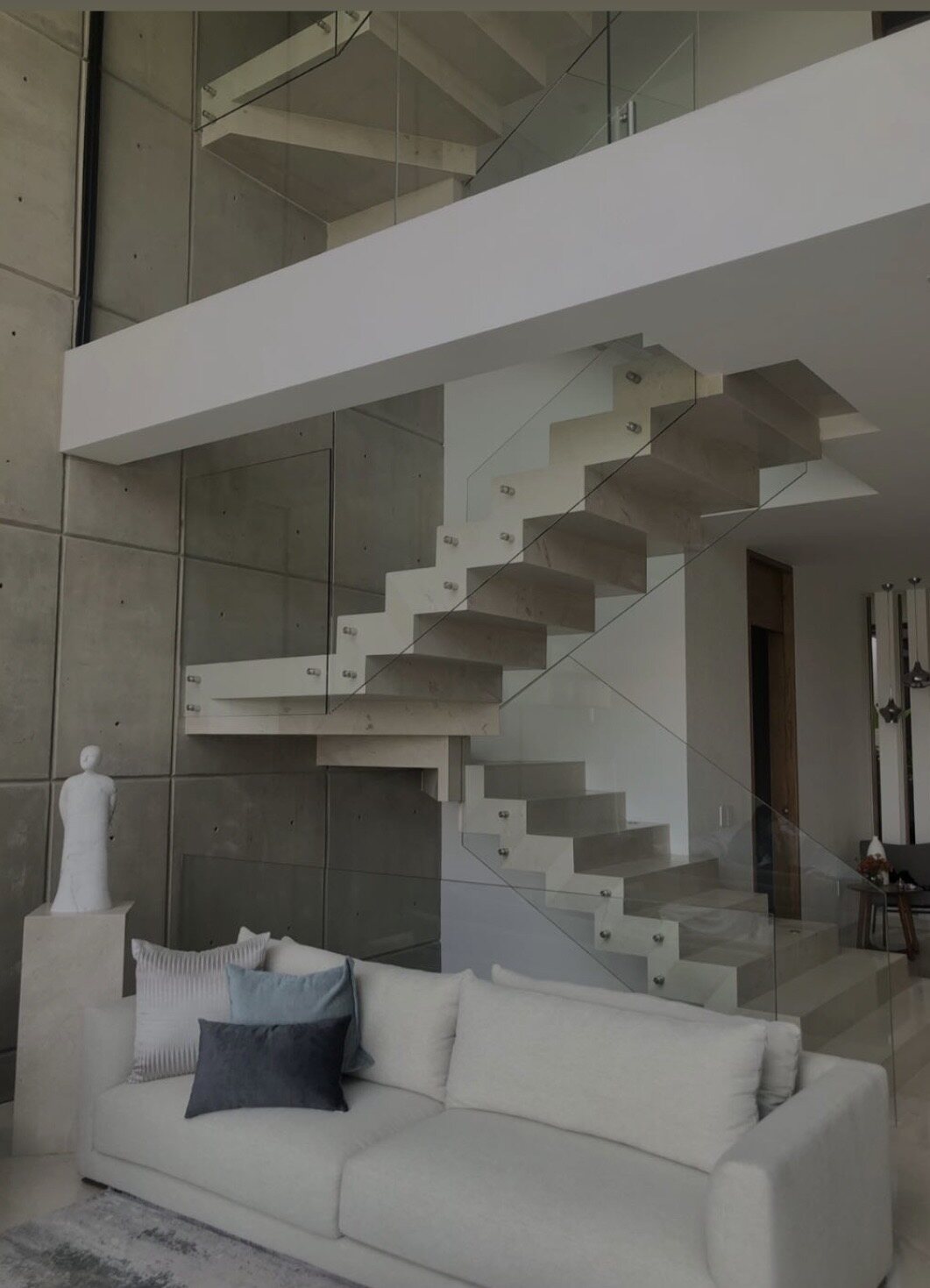 A floating cast-concrete stair beside a white sofa in a double-height room.